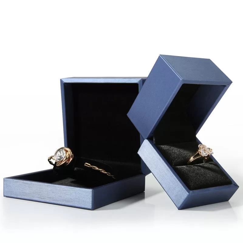 Open teal jewelry box displaying diamond ring on black velvet background.