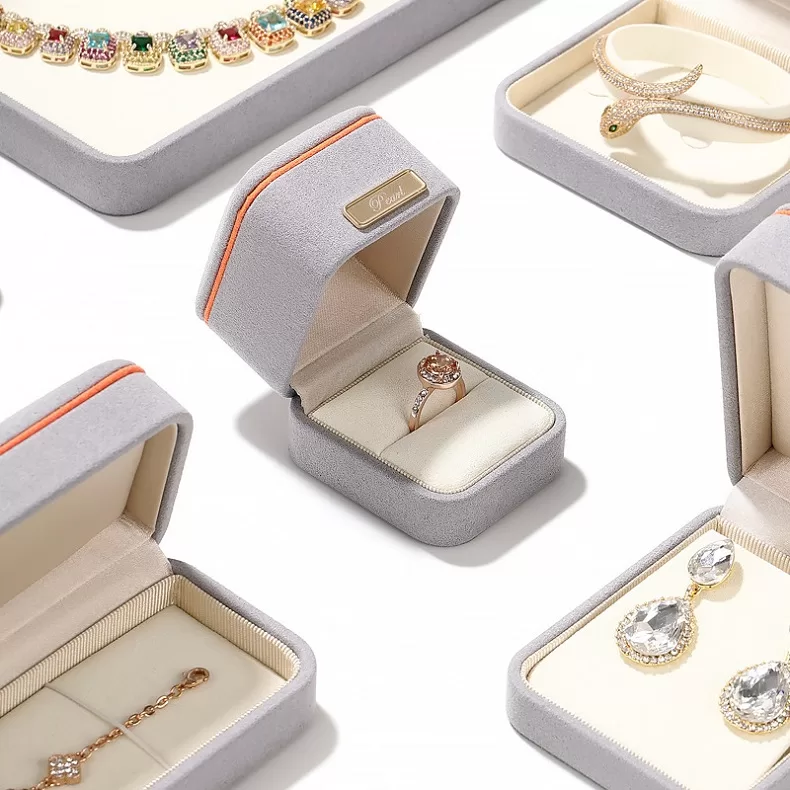 Light grey microfiber ring box with orange trim and gold bar detail