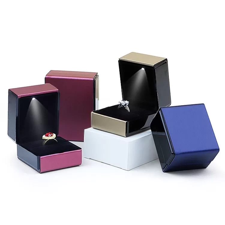 Open LED engagement ring box illuminating diamond ring on black velvet.