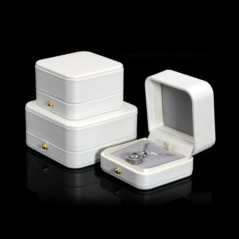 Close up of gold press stud on white leather engagement ring box.